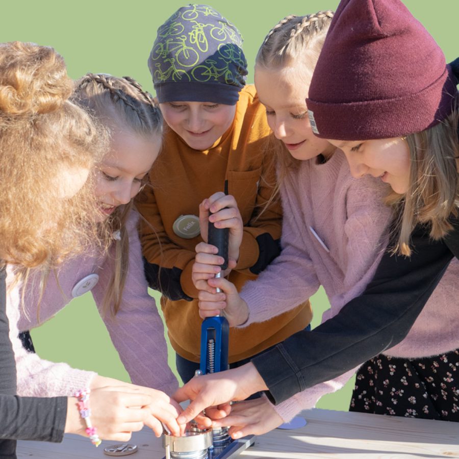 Event kids create organic buttons with button machine in nature with green background